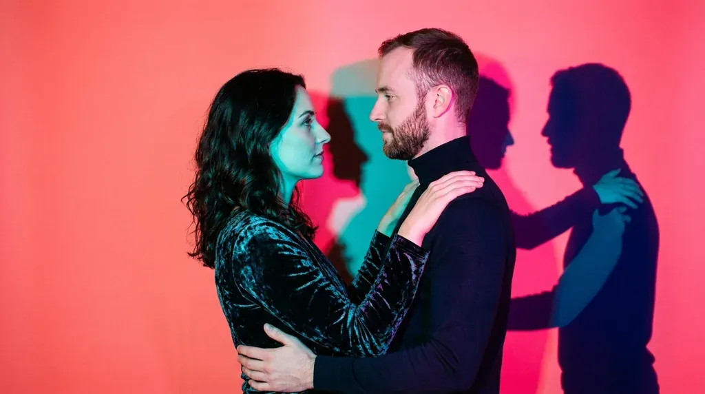 Photographie éditoriale d'un couple attablé, éclairé de magenta et de cyan, séparé par une longue ombre projetée sur la table