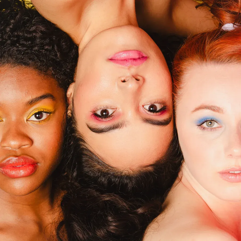 Visages de femmes diverses serrés côte à côte, maquillages colorés