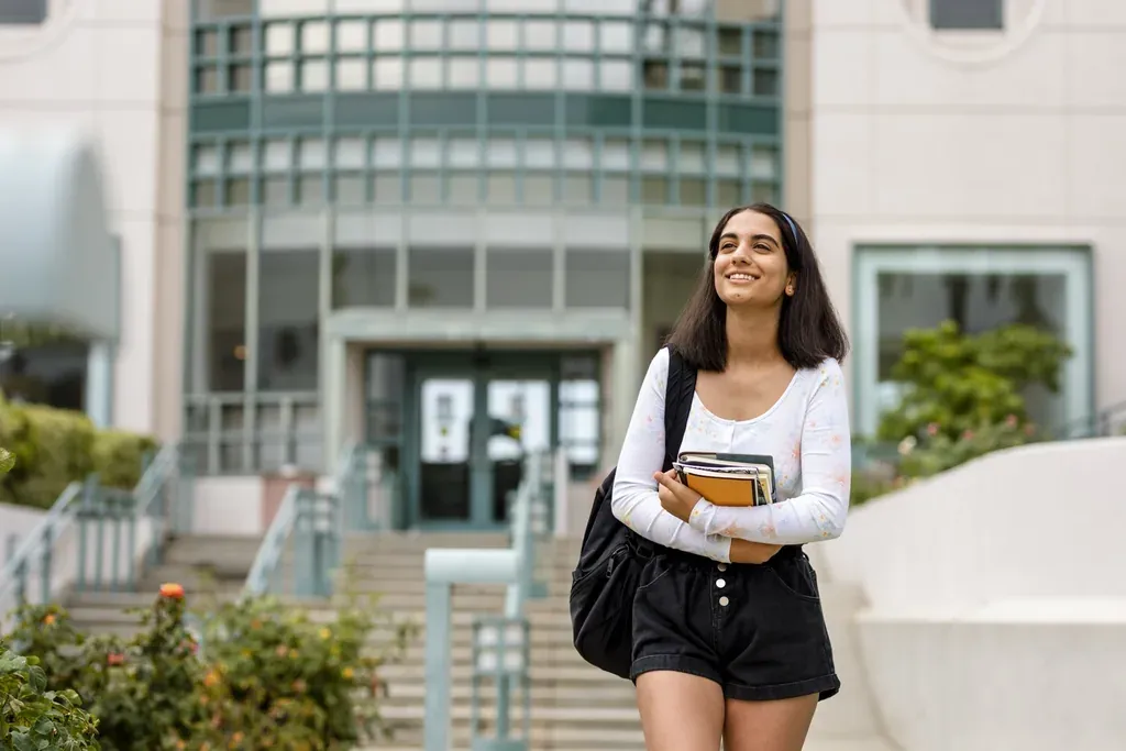 Étudiante souriante, livres en main, devant l'entrée d'une université