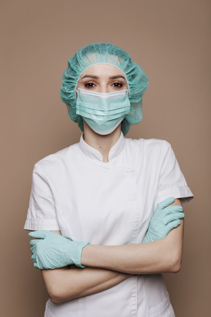 Soignante en tenue chirurgicale, masque et gants, bras croisés, regard direct