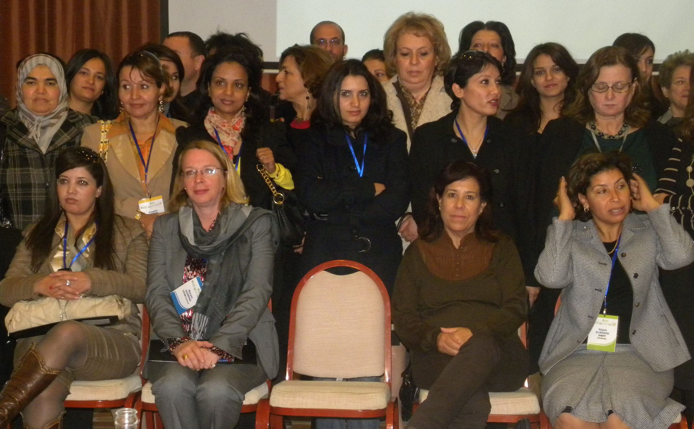 Une salle remplie de femmes tunisiennes assises et debout, badges au cou, lors d'un forum de consultation
