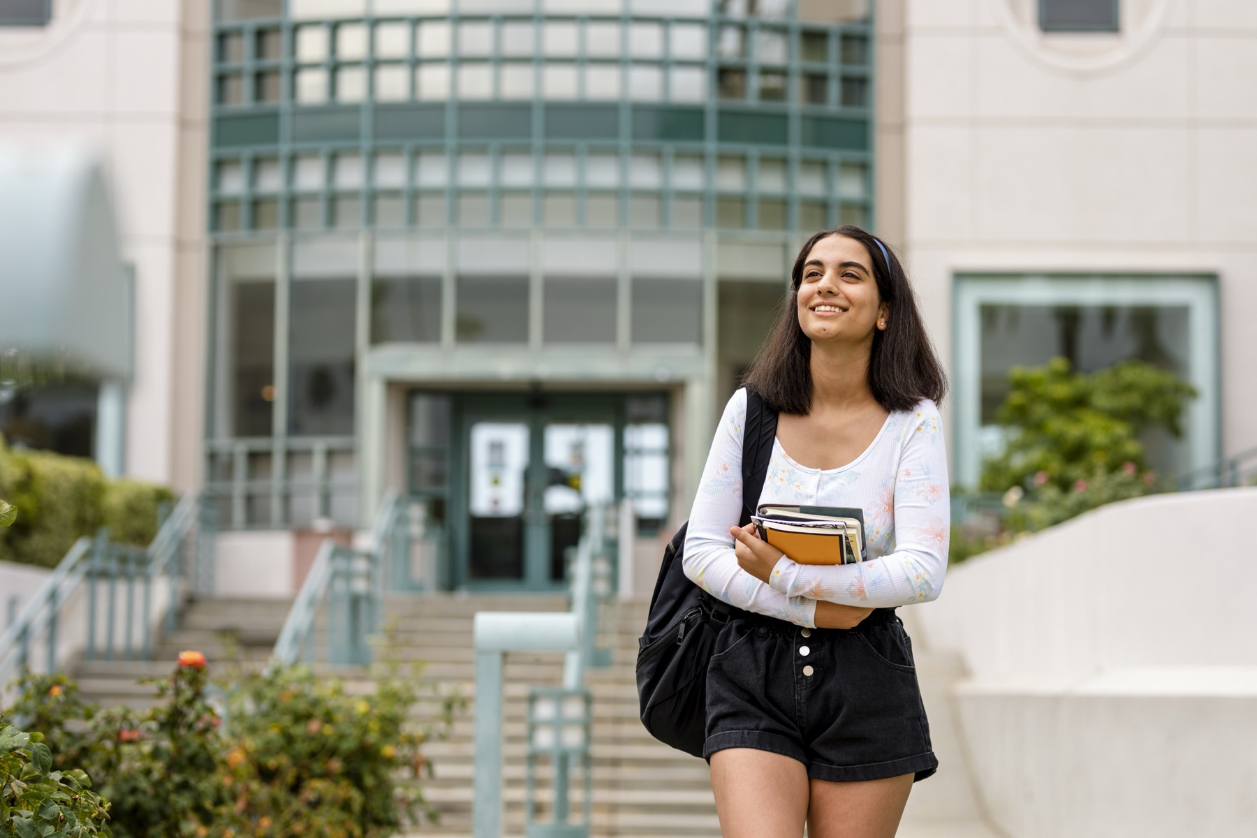 Étudiante souriante, livres en main, devant l'entrée d'une université