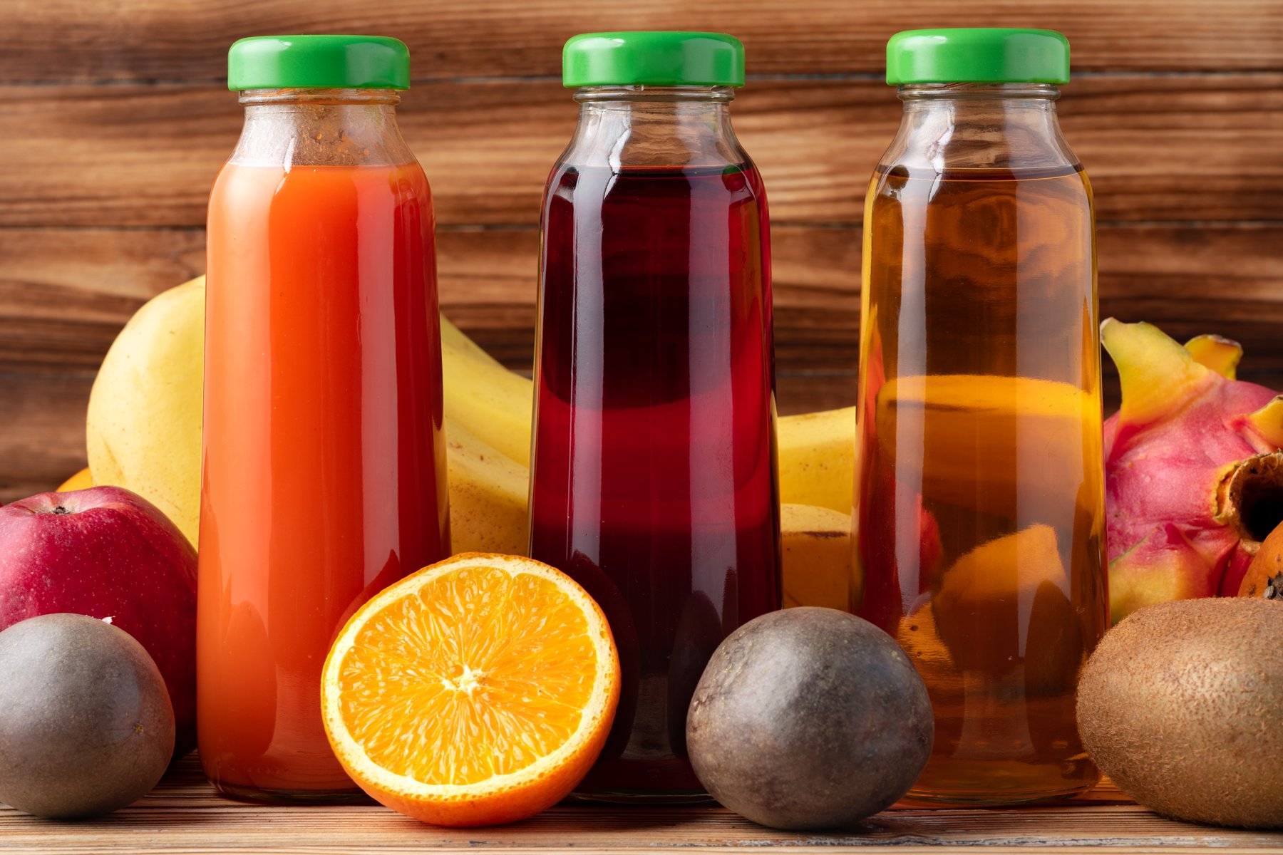 Jus de fruits frais en bouteilles, entourés de fruits sur une table de bois